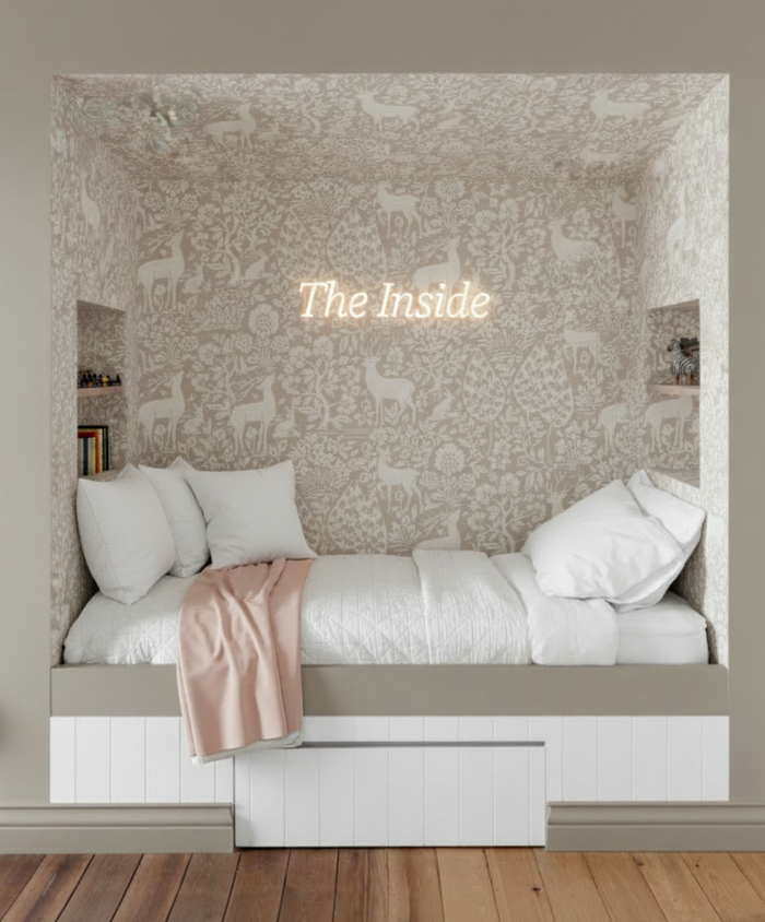 Bedroom nook with Deer Woods pink wallpaper, pink blanket, and The Inside neon sign