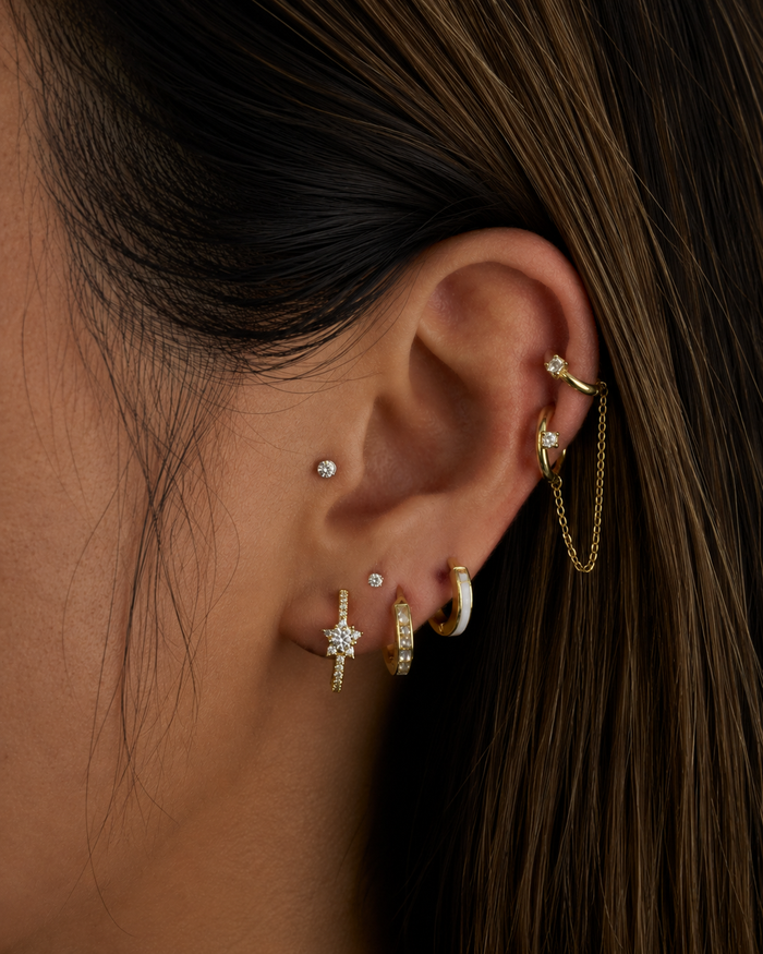 Close-up of an ear with multiple gold and diamond earrings against a dark background