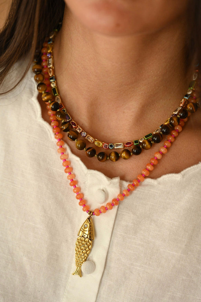 Necklace with colorful beads and a gold fish pendant on a white shirt