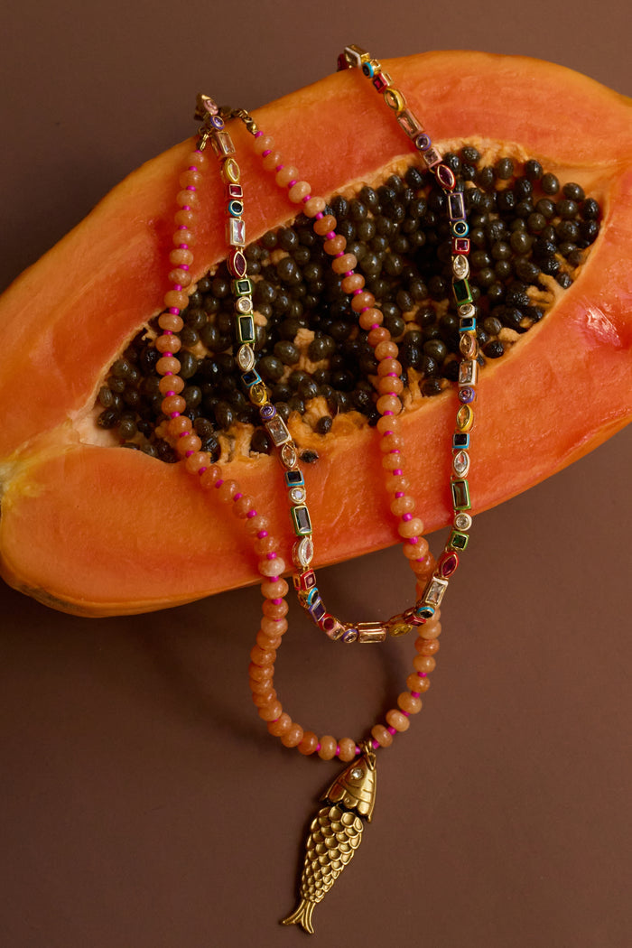 Beaded necklaces with a fish charm on a halved papaya.
