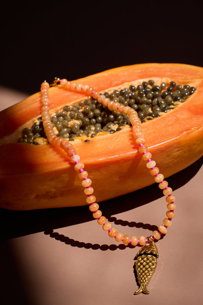 Necklace with a fish charm draped over a halved papaya on a dark background