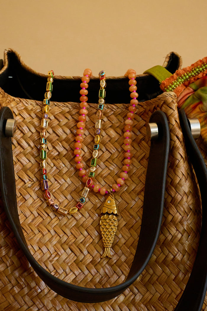 Woven bag with colorful beaded necklace and fish pendant on a beige background