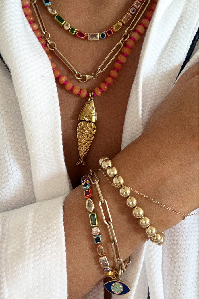 Close-up of a person wearing multiple necklaces and bracelets with colorful beads and gold accents.