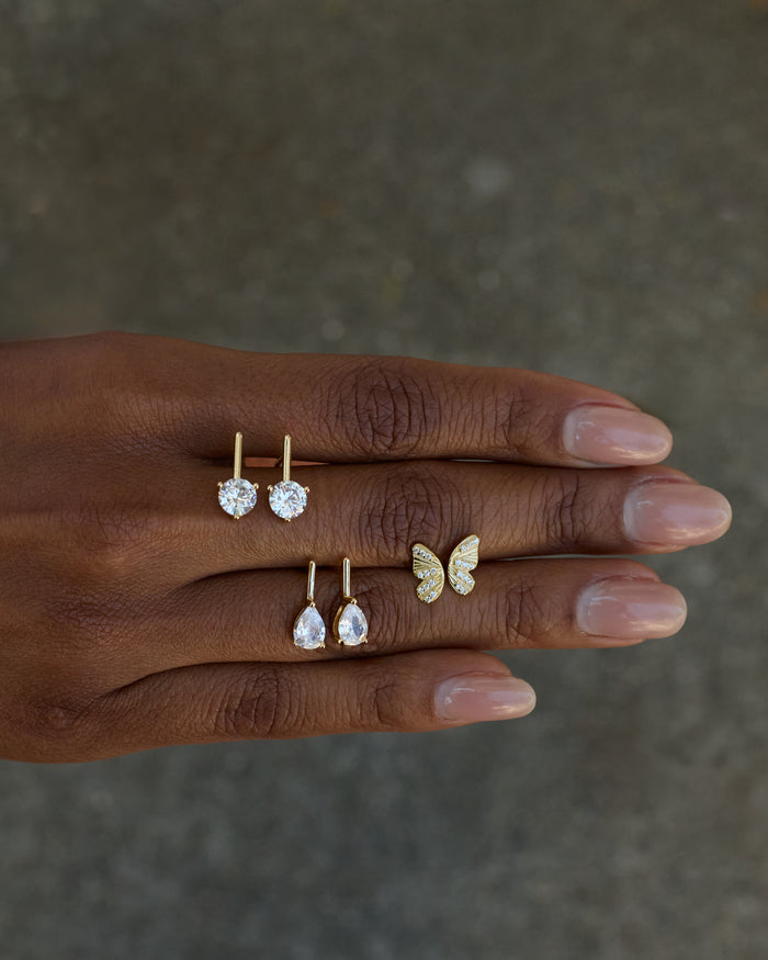 Hand wearing gold butterfly ring and earrings on a neutral background