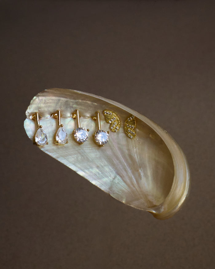 Set of gold and diamond earrings on a shell against a brown background