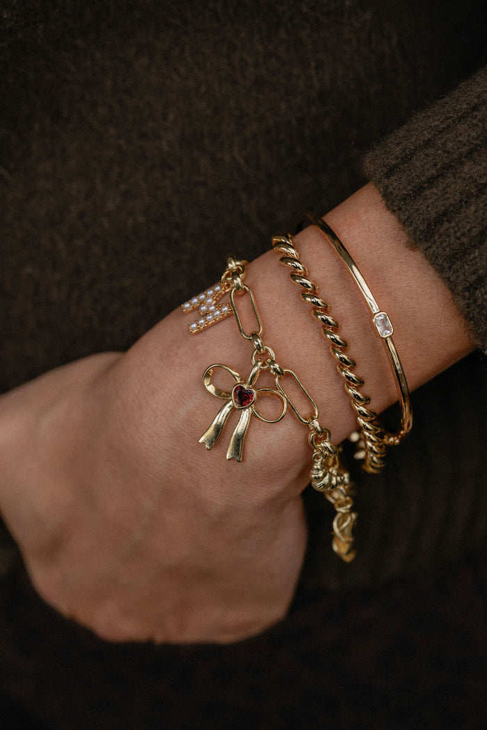Gold bracelets with charms on a wrist against a dark background