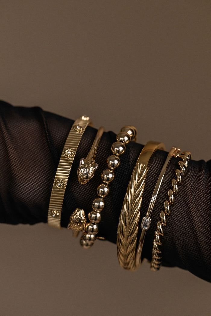 Collection of gold bracelets on a black mesh sleeve