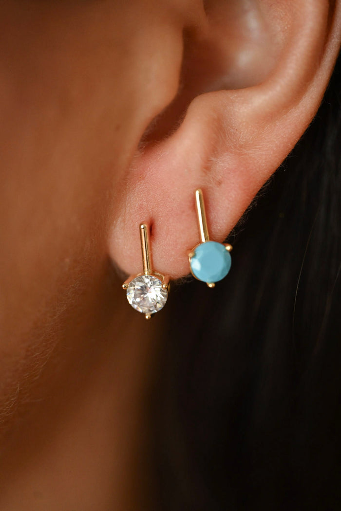 Close-up of an ear wearing two gold earrings with gemstones.